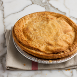 A golden-brown baked pie on a metal tray resting on a folded beige cloth, set on a white marble surface.