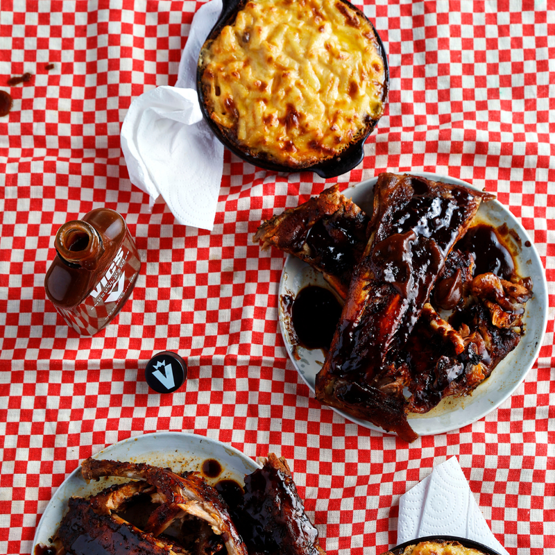 Bbq ribs on a checkered tablecloth with a bottle of sauce