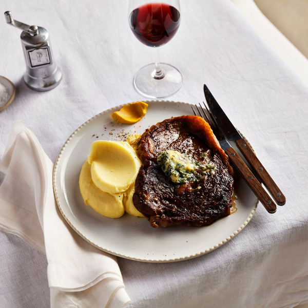 Steak with mashed potatoes and a glass of red wine on a white tablecloth.