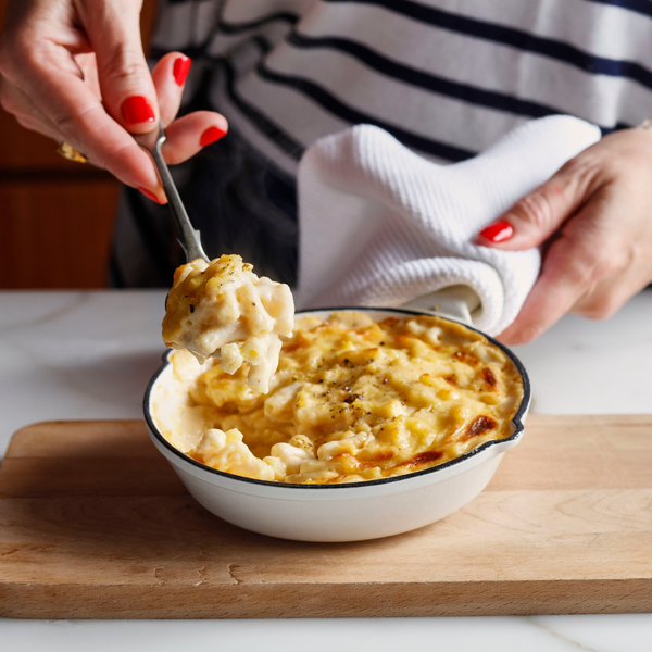 Person serving macaroni and cheese from a bowl on a wooden cutting board.