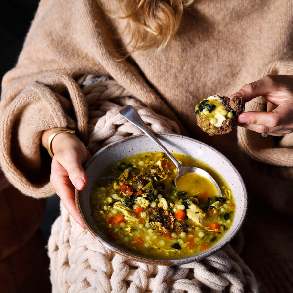 Person holding a bowl of soup with a spoon and a piece of bread, wearing a cozy sweater.