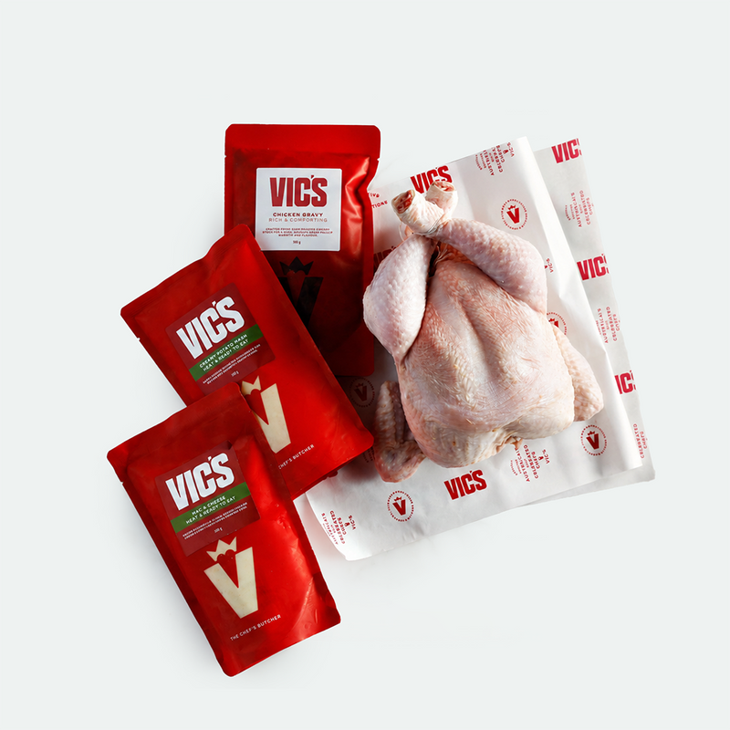 Three red VICS pouches of chicken seasoning rub and a whole raw chicken placed on branded white VICS paper packaging, arranged on a light gray background.